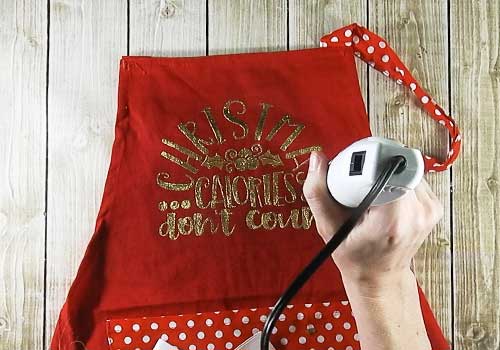 Make this cute heat embossed Apron for Christmas with this easy to follow tutorial. With a few tools and your Silhouette or Cricut machine, you'll be able to create this heat embossed Apron. This DIY project is easy and quick to make and is the perfect decoration for home. #ChristmasSilhouette #ChristmasCricut #ChristmasSVG